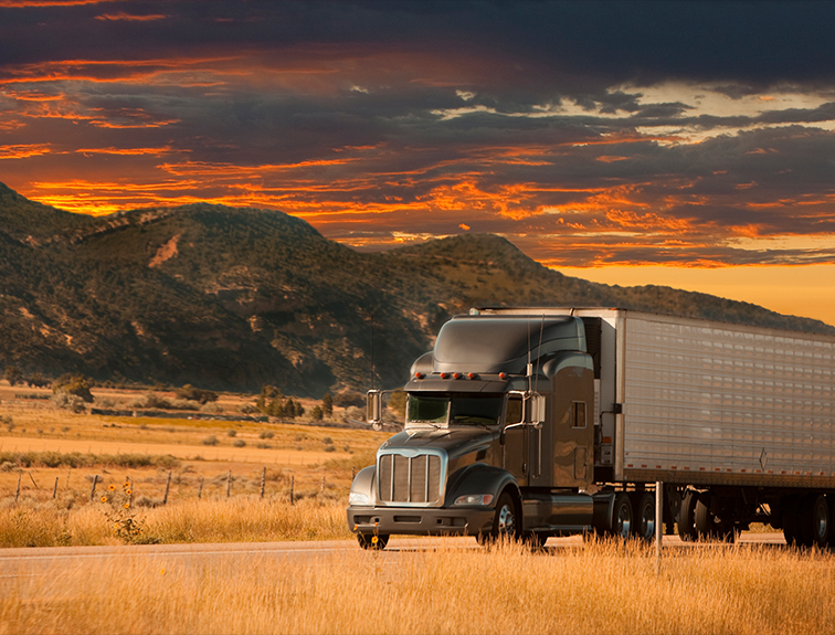semi truck driving with mountains and sunset behind them
