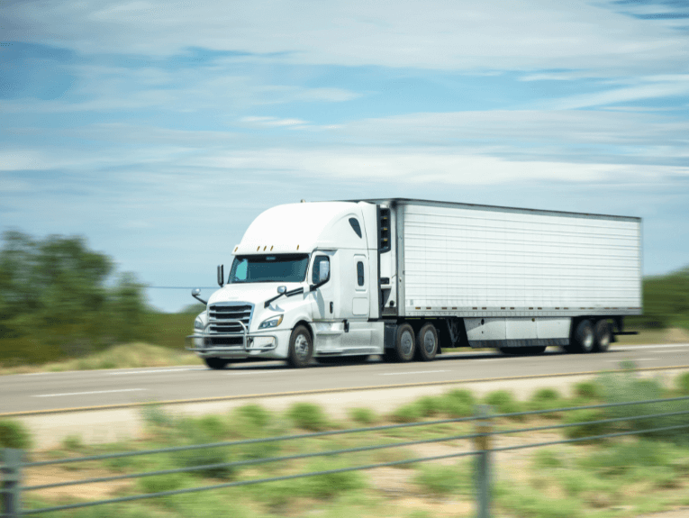 image of white tractor trailer driving on highway, blurred to show motion
