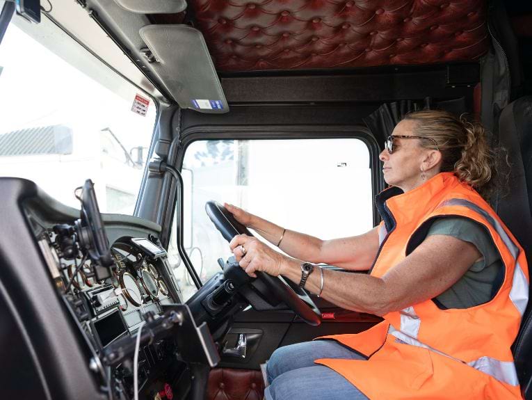 Image of a woman wearing an orange safety vest while learning to drive a semi truck.