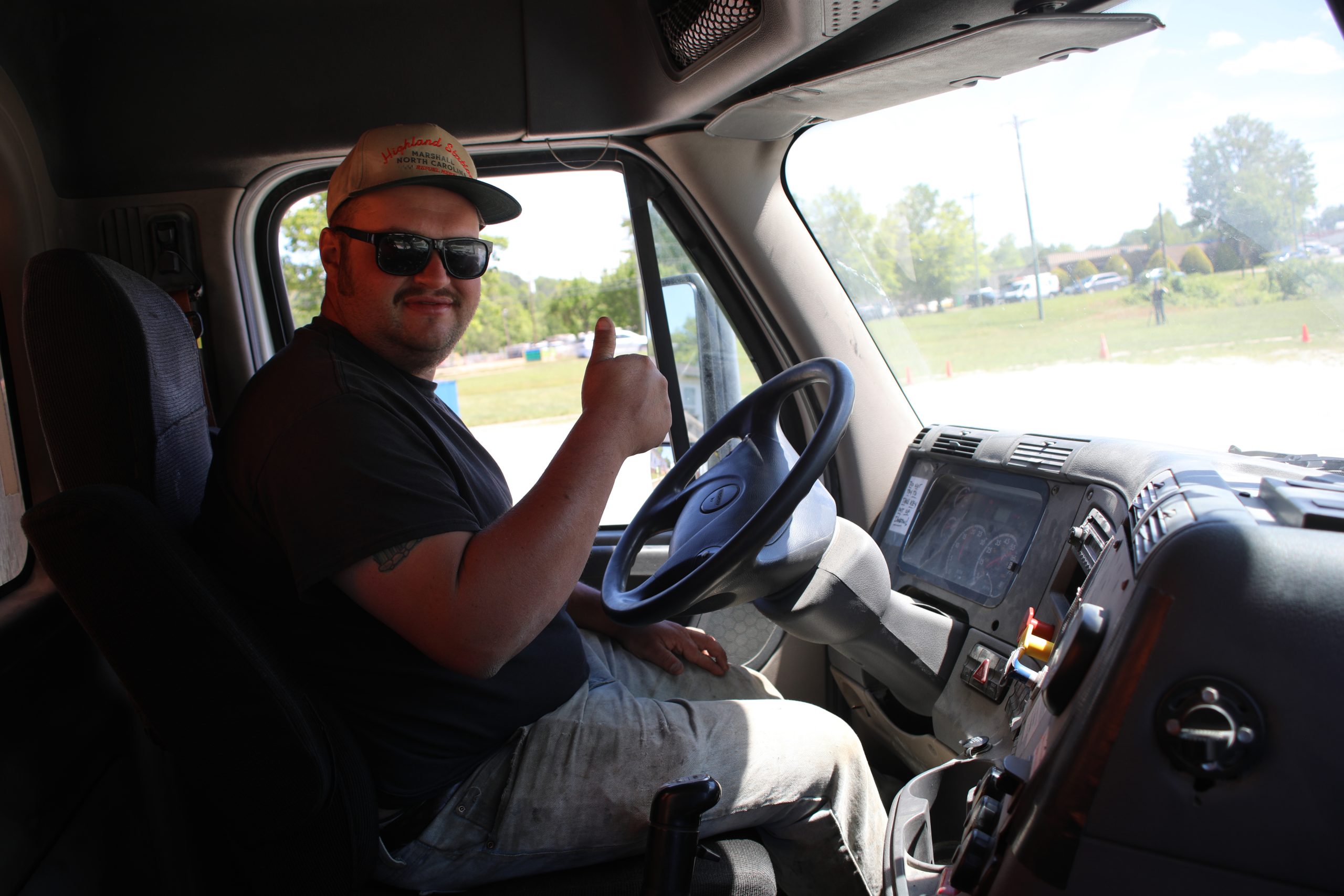 Trucker sitting behind wheel of semi truck holding up a thumbs up