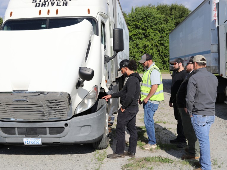 Group of CDL students looking inside the engine cab of a semi truck on a training yard